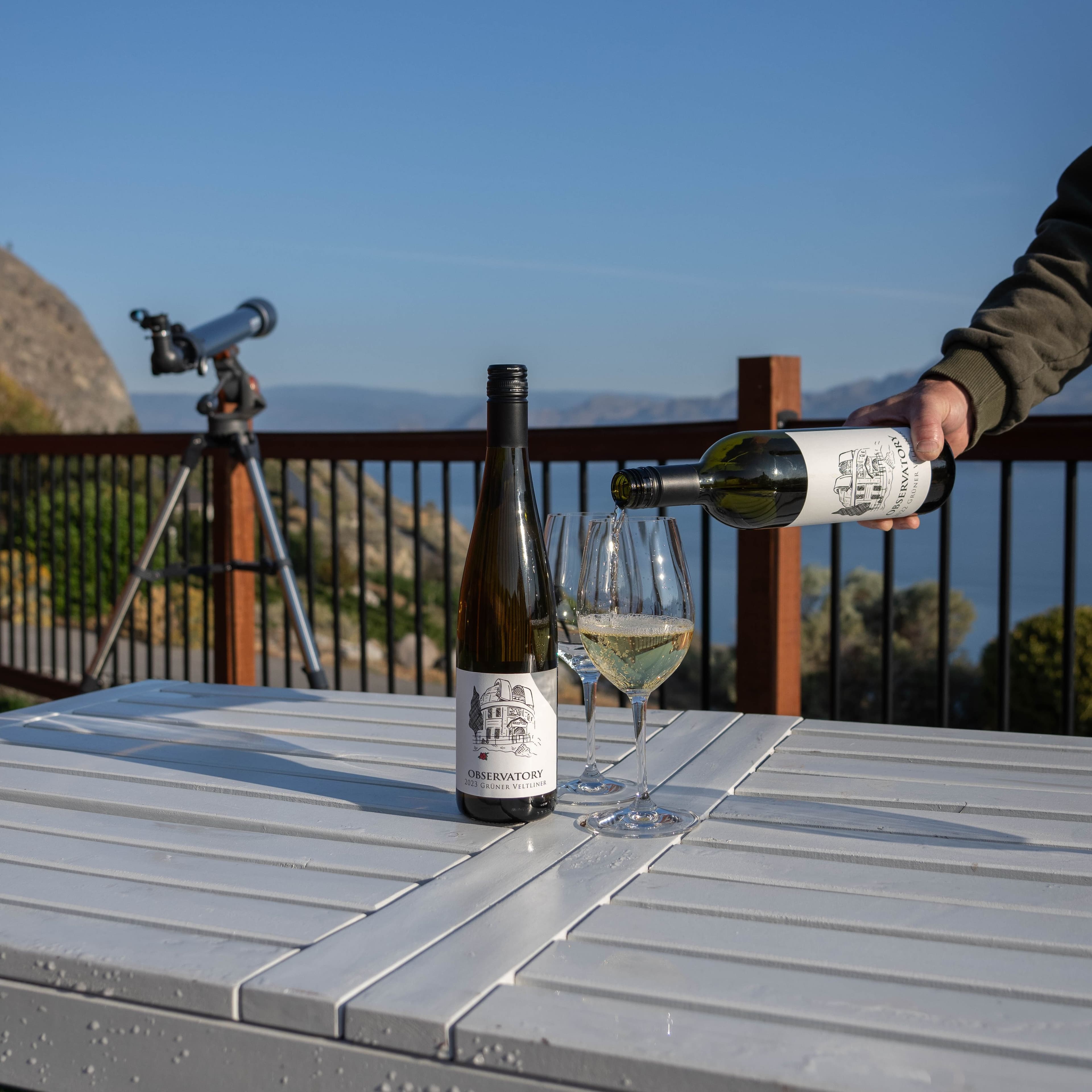 Observatory wine being poured into glasses on outdoor deck with telescope and lake view